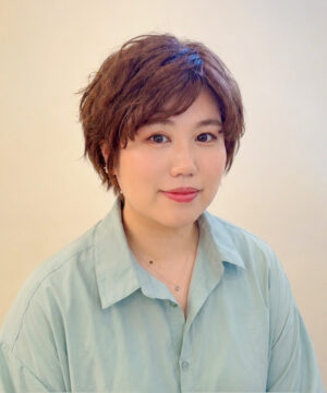 Portrait of a person with short brown hair and a pale blue shirt, facing the camera with a gentle smile.